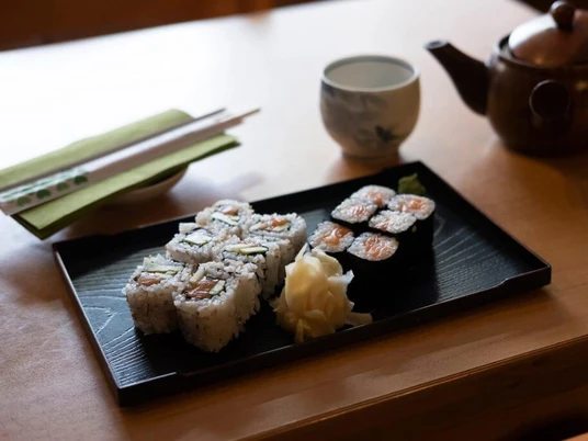 Fisch Hof Sushi Haus Sushi präsentiert auf einem schwarzen Teller. Im Hintergrund eine Kupferteekanne.Sushi presented on a black plate. In the background, a copper teapot.