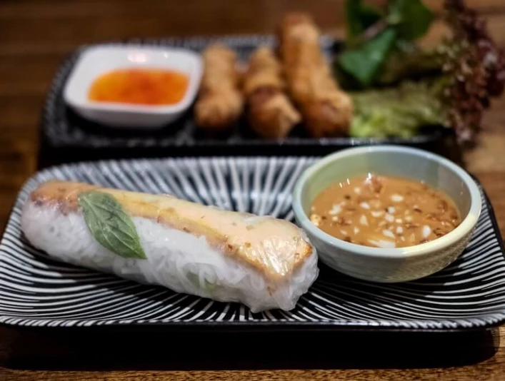 Restaurant Lua by Danny Nahaufnahme einer Sommerrolle mit einem Schälchen Erdnusssoße. Close-up of a summer roll with a small bowl of peanut sauce.