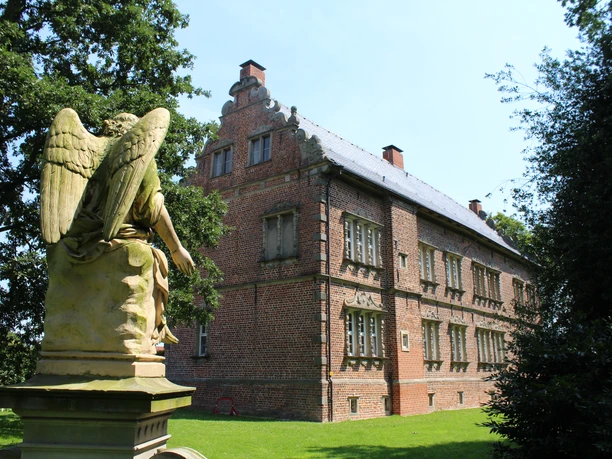 Thedinghausen Schloss Erbhof Backstein-Schloss Erbhof in Thedinghausen mit Engelsstatue im Vorgarten, umgeben von grünen Bäumen.
