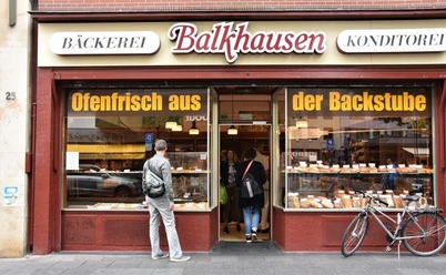 Bäckerei Balkhausen Außenansicht auf die Bäckerei. Ein Mann schaut auf das mit Backwaren bestückte Schaufenster.