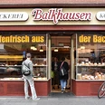 Bakery Balkhausen Außenansicht auf die Bäckerei. Ein Mann schaut auf das mit Backwaren bestückte Schaufenster. Exterior view of the bakery. A man looks at the shop window filled with baked goods.