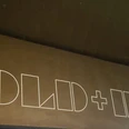 GOLD + BETON Das Bild zeigt eine Wand mit dem Schriftzug "GOLD + BETON" in weiß auf einem gold-braunen Hintergrund.Signboard displaying 'GOLD + BETON' in bold white letters, set against a dark wooden backdrop.
