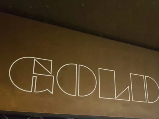 GOLD + BETON Das Bild zeigt eine Wand mit dem Schriftzug "GOLD + BETON" in weiß auf einem gold-braunen Hintergrund.Signboard displaying 'GOLD + BETON' in bold white letters, set against a dark wooden backdrop.