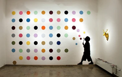 30works Galerie In einem weißen Raum ist eine Installation zu sehen, die aus einer Wand mit bunten Punkten besteht. Daneben die Silhouette eines Kindes, das Blasen pustet, und eine goldene Hirschkopfskulptur.