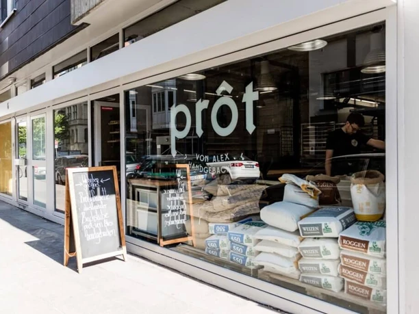 prôt A modern bakery with large windows showcasing various flour sacks on the ground floor.
