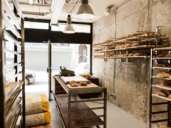 prôt Eine kleine Bäckerei mit rustikaler Backsteinwand und Regalen voller frisch gebackener Brote und Brötchen.A small bakery featuring rustic brick walls and shelves filled with freshly baked breads and rolls.