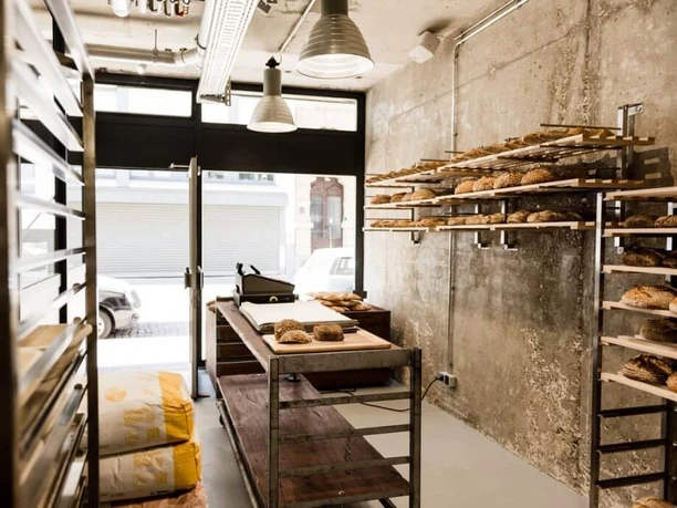 prôt A small bakery featuring rustic brick walls and shelves filled with freshly baked breads and rolls.