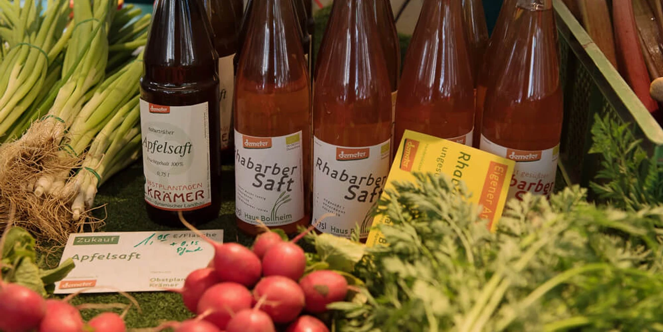 wochenmaerkte_koeln_rudolfplatz-2.jpg Auf einem Marktstand stehen verschiedene Flaschen Rhabarber- und Apfelsaft. Daneben frisches Gemüse wie Lauchzwiebeln, Radieschen und Rote Beete.There are various bottles of rhubarb and apple juice on a market stall. Next to them are fresh vegetables such as spring onions, radishes and beet.