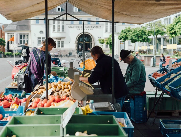 Weekly market on Neptunplatz Marktstände auf dem Neptunplatz in Köln unter einem großen Pavillon. Menschen kaufen frisches Obst und Gemüse.Market stalls on Neptunplatz in Cologne under a large pavilion. People buy fresh fruit and vegetables.