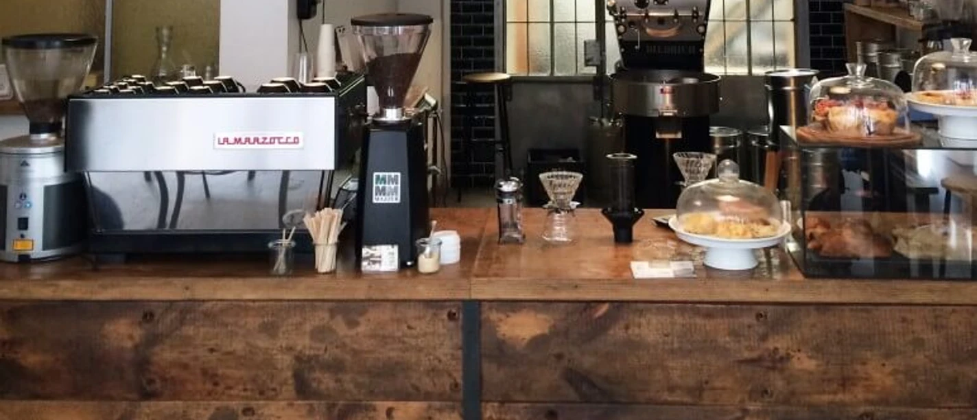 ERNST KAFFERÖSTER An industrial-style counter with a cake display and an espresso machine.