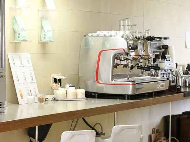 VAN DYCK Espressobar Eine moderne Kaffeerösterei mit silberner Espressomaschine, Barhockern und gemütlicher Atmosphäre.