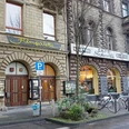 Filmpalette Ansicht des Filmtheaters "Filmpalette" in Köln, eingefasst von historischen Steingebäuden, bei grauem Wetter.The image shows the entrance of "Filmpalette", a cosy cinema located in a historic building with an ornate facade, next to a vibrant café. Bicycles are parked along the pavement, fostering a lively street atmosphere.