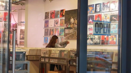 Parallel Schallplatten Ein Schallplattenladen mit offenen Türen zeigt eine Person, die im Inneren Schallplatten durchstöbert.