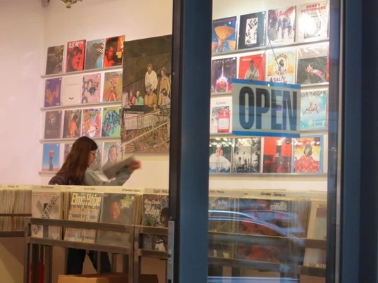 Parallel Schallplatten Ein Schallplattenladen mit offenen Türen zeigt eine Person, die im Inneren Schallplatten durchstöbert.A record store with open doors shows a person browsing through records inside.