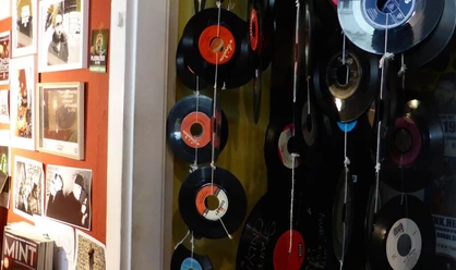 Early Bird Records Vinyl-Schallplatten hängen dekorativ an Schnüren vor einer roten Wand voller Musikposter.
