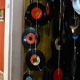 Early Bird Records Vinyl-Schallplatten hängen dekorativ an Schnüren vor einer roten Wand voller Musikposter.Vinyl records hang decoratively on strings in front of a red wall full of music posters.