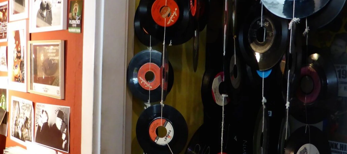 Early Bird Records Vinyl-Schallplatten hängen dekorativ an Schnüren vor einer roten Wand voller Musikposter.Vinyl records hang decoratively on strings in front of a red wall full of music posters.