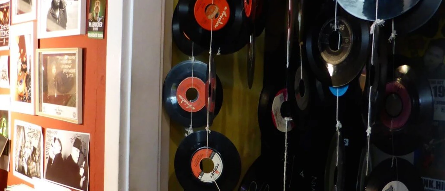Early Bird Records Vinyl records hang decoratively on strings in front of a red wall full of music posters.