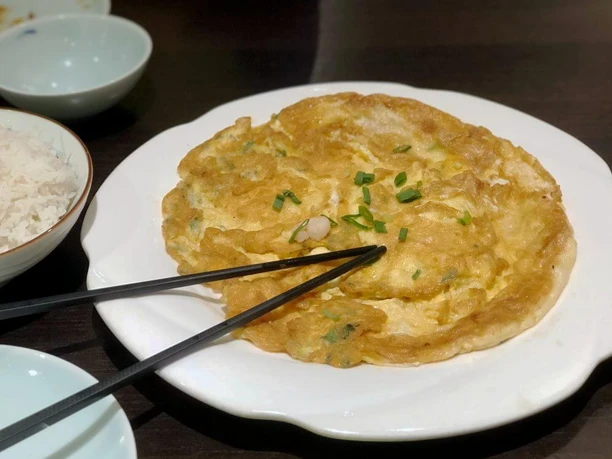 Tang Wang Goldbraunes Omelett mit Frühlingszwiebeln auf einem weißen Teller, daneben Essstäbchen.