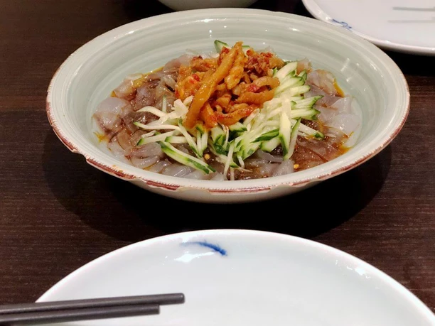 Tang Wang Auf dem Bild ist eine Schale mit kalten Glasnudeln, Gurkenstreifen und knusprigen Toppings in einer Soße zu sehen.