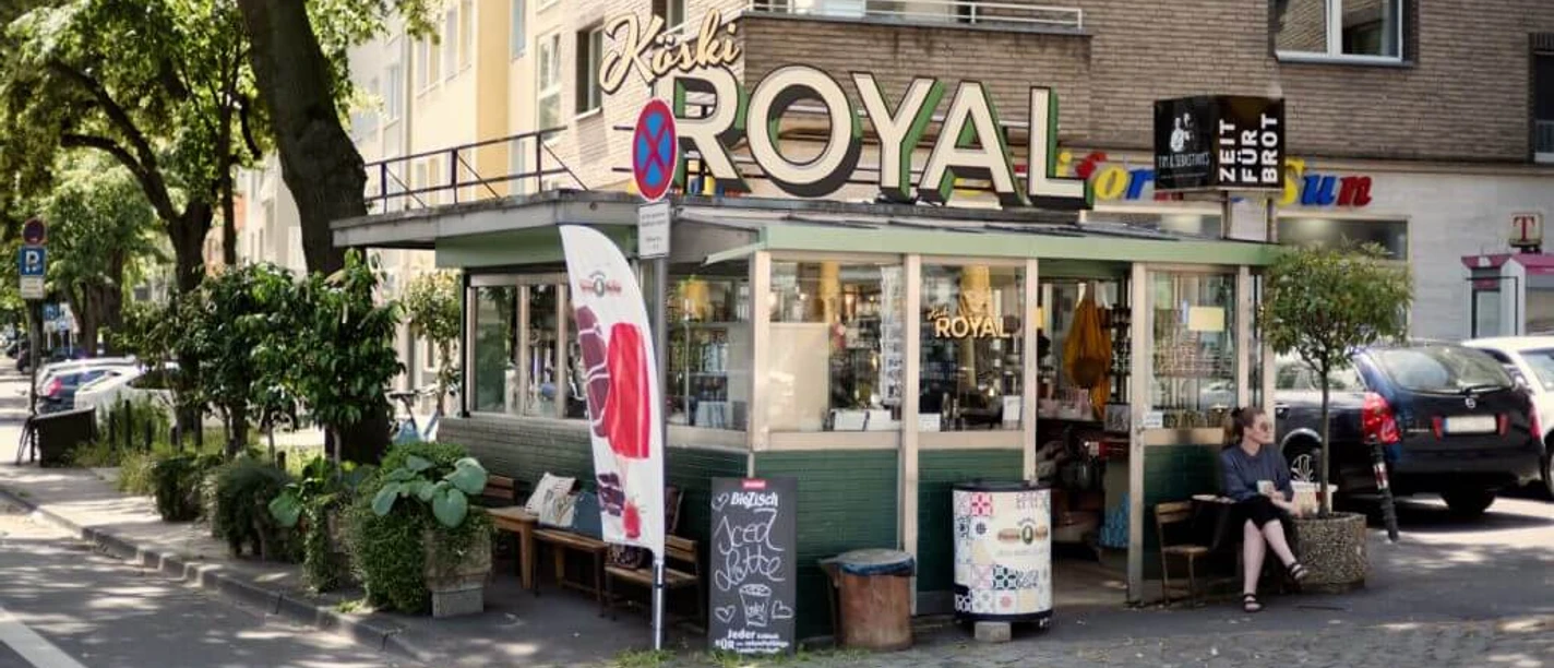 Köski Royal A charming kiosk with the lettering "KÖSKI ROYAL", surrounded by urban greenery in an urban environment.