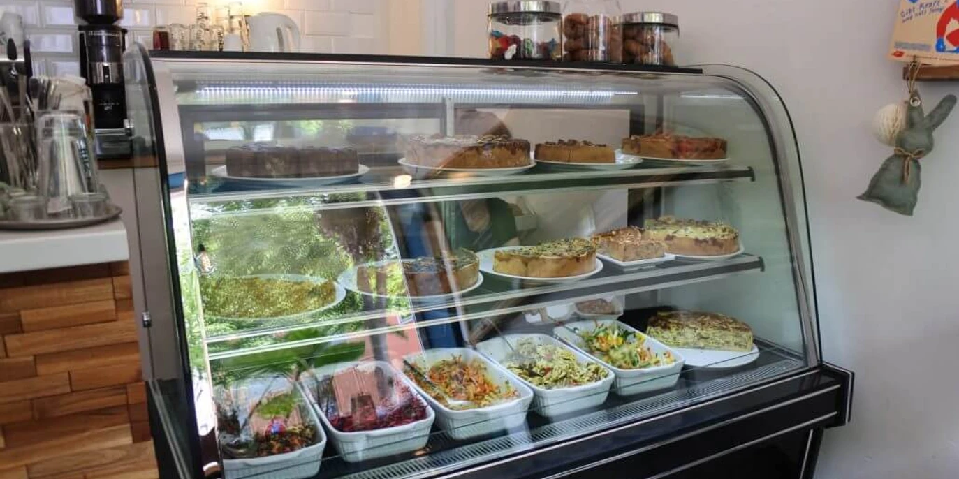 Cafe Frau Maaß Herr Schlie Glasvitrine mit herzhaften Quiche und Salaten. Glass display case with savory quiche and salads.
