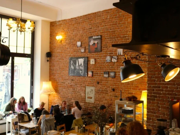 Wohnraum Cozy café featuring brick walls, large windows, and sociable guests seated around tables.