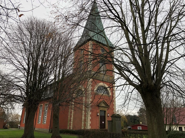 Church in the village of Intschede, surrounded by bare trees in the fall, with a striking green church tower.