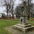 Herzog-Wilhelm Denkmal in einem grünen Park, umgeben von herbstlichen Bäumen und Gebäuden im Hintergrund.