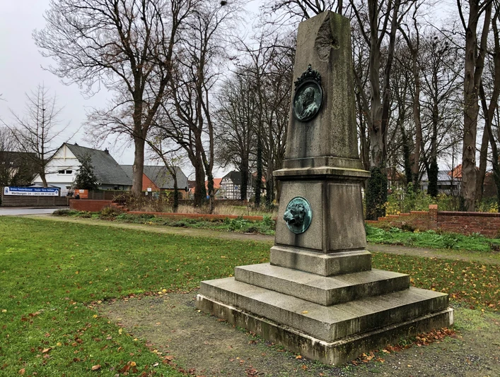 Herzog-Wilhelm Denkmal in einem grünen Park, umgeben von herbstlichen Bäumen und Gebäuden im Hintergrund.