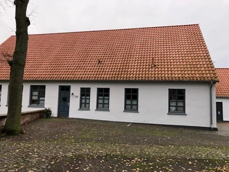 Küsterhaus Daverden Ein einstöckiges Haus mit roten Ziegeln und weißen Wänden, umgeben von einer steinernen Terrasse.