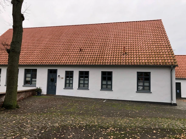 Küsterhaus Daverden Ein einstöckiges Haus mit roten Ziegeln und weißen Wänden, umgeben von einer steinernen Terrasse.