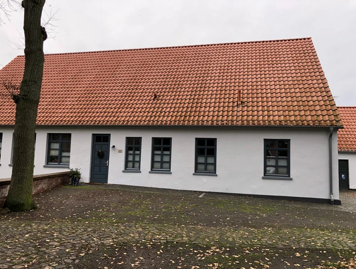 Küsterhaus Daverden Ein einstöckiges Haus mit roten Ziegeln und weißen Wänden, umgeben von einer steinernen Terrasse.