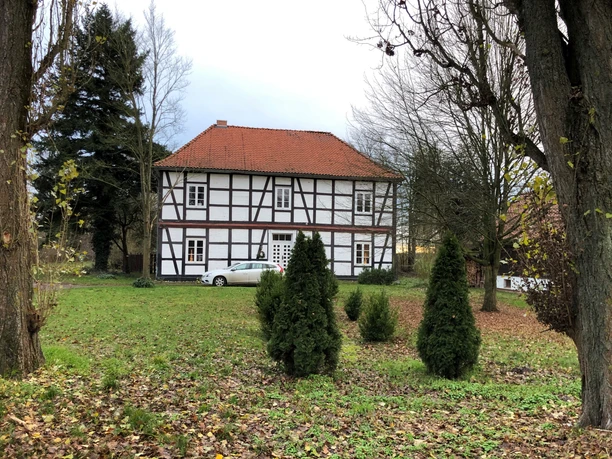 Amtshaus Wölpe Fachwerkhaus inmitten von Bäumen mit roten Dachschindeln und einem Auto davor auf grüner Wiese.
