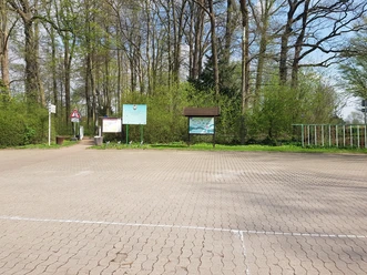 Parkplatz am Sportplatz Bad Holzhausen Leerer Parkplatz mit umliegenden Schildern und Bäumen im Hintergrund, nahe einem Waldweg gelegen.