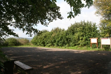 Wanderparkplatz "Holzhauser Berg" Wanderparkplatz Holzhauser Berg mit Bank im Vordergrund, umgeben von dichten Bäumen und Sträuchern.