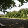 Wanderparkplatz "Holzhauser Berg" Wanderparkplatz Holzhauser Berg mit Bank im Vordergrund, umgeben von dichten Bäumen und Sträuchern.