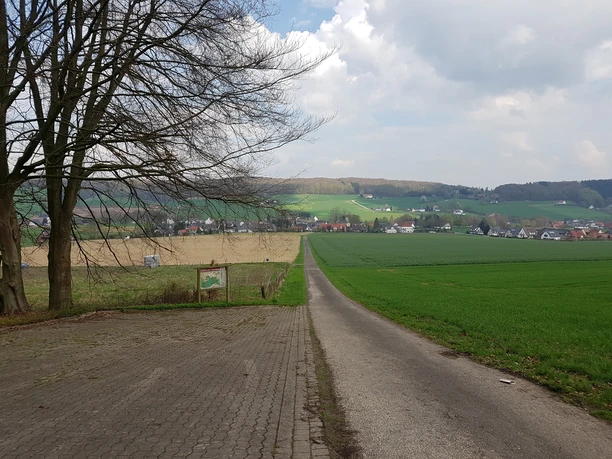 Wanderparkplatz Nonnensteiner Weg Zugang zum Wanderweg mit Blick auf eine ruhige Landschaft aus Feldern und entfernten Hügeln.