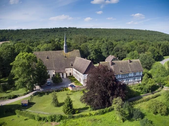 Luftaufnahme des Klosters Falkenhagen inmitten grüner Wälder unter einem klaren blauen Himmel.