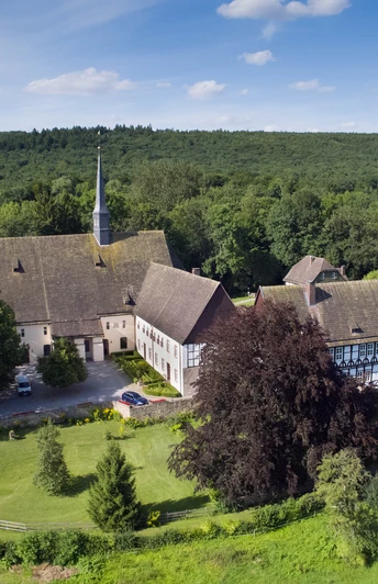 Luftaufnahme des Klosters Falkenhagen inmitten grüner Wälder unter einem klaren blauen Himmel.
