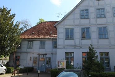 SG Grafschaft Hoya Heimatmuseum Historisches weißes Fachwerkgebäude mit rotem Ziegeldach, bunten Fenstern und grünem Baum im Vordergrund.