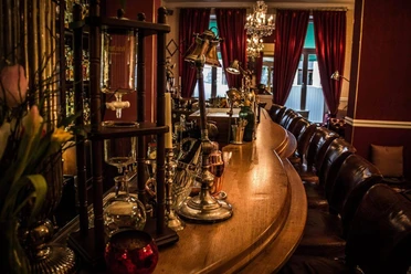 Seiberts Cocktailbar Eine gemütliche Cocktailbar mit einer eleganten Holztheke, umgeben von Lampen und Sitzgelegenheiten. Die Atmosphäre ist einladend und stilvoll.