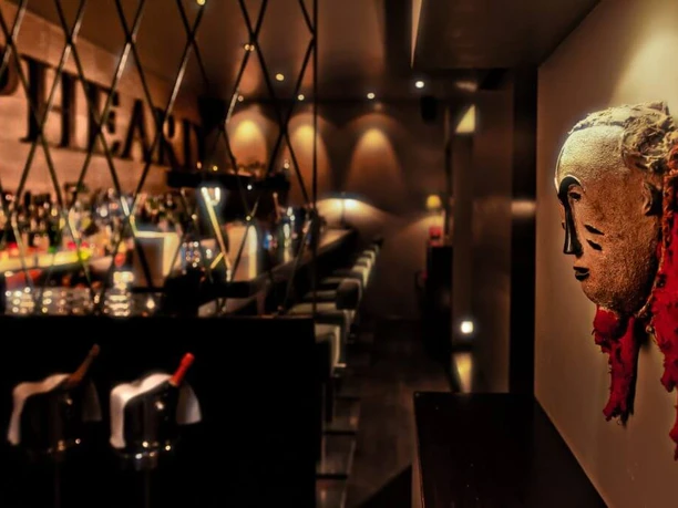 Samuel's Shep A stylish bar featuring an artistic mask on the wall. Elegantly illuminated, the bar invites guests for a relaxed evening.