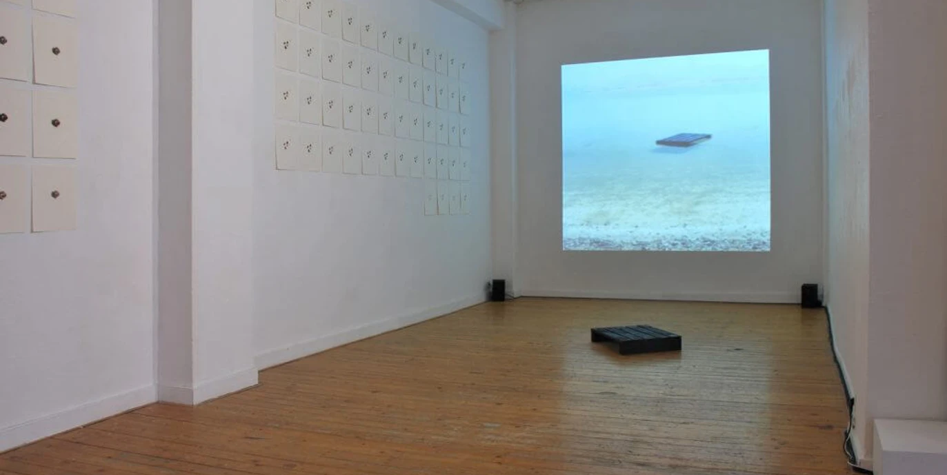 Moltkerei Werkstatt In einem minimalistisch gestalteten Raum sind auf hellem Holzboden eine Projektion und an Wänden befestigte Blätter zu sehen.In a room with a minimalist design, a projection and leaves attached to the walls can be seen on a light-colored wooden floor.