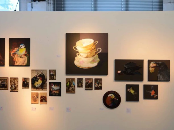 artrmx e. V. | Atelierzentrum Ehrenfeld Verschiedene Kunstwerke hängen leicht ungleichmäßig an einer weißen Wand in einer Galerie.