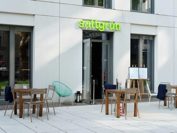 Sattgrün Außenansicht eines modernen veganen Restaurants mit heller Fassade, stilvollen Holztischen und Stühlen auf einer großzügigen Terrasse.