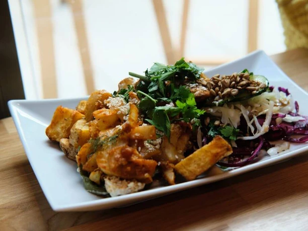 Sattgrün A rectangular plate attractively arranged with a vegetarian meal. On the left side are crispy fried tofu pieces garnished with an herbal sauce. On the right side is a crunchy, vibrant salad mix of red cabbage, white cabbage, arugula, and sunflower seeds, appearing fresh and colorful.