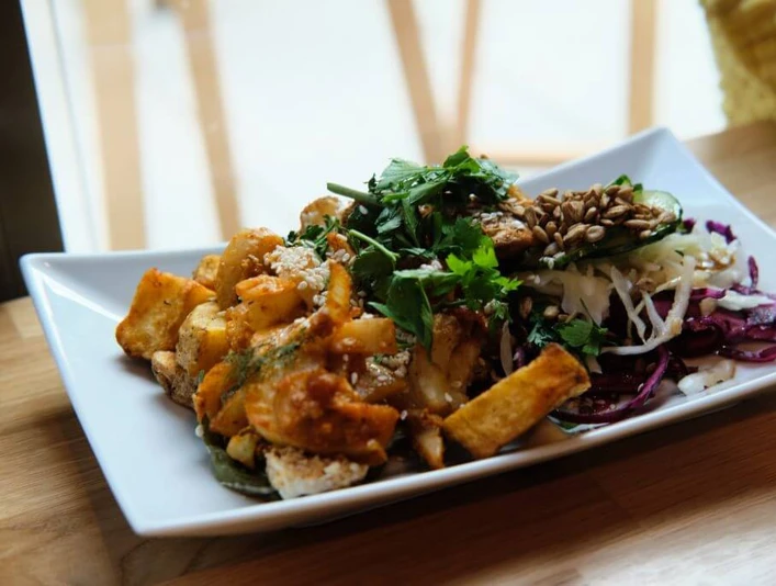 Sattgrün Ein rechteckiger Teller mit einer ansprechend angerichteten vegetarischen Mahlzeit. Links auf dem Teller befinden sich knusprig gebratene Tofu-Stücke, garniert mit einer Kräutersauce. Rechts ist ein knackiger, bunter Salatmix aus Rotkohl, Weißkohl, Rucola und Sonnenblumenkernen zu erkennen, der frisch und farbenfroh wirkt.A rectangular plate attractively arranged with a vegetarian meal. On the left side are crispy fried tofu pieces garnished with an herbal sauce. On the right side is a crunchy, vibrant salad mix of red cabbage, white cabbage, arugula, and sunflower seeds, appearing fresh and colorful.