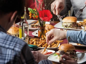 Die fette Kuh Burger Nahaufnahme von Tellern mit Burgern und Pommes. Eine Hand tunkt eine Pommes in Ketchup. Close-up of plates with burgers and fries. A hand dips a French fry into ketchup.