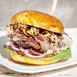 Die fette Kuh Burger A burger with bacon, popcorn, onions, salad and a patty.